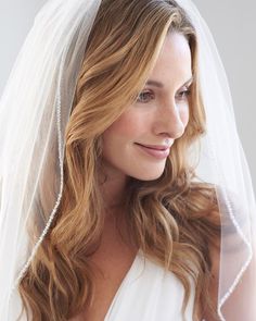 a woman wearing a wedding veil with pearls on the head and shoulder is looking to her left