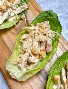 two lettuce leaves with chicken and cheese on them sitting on a cutting board