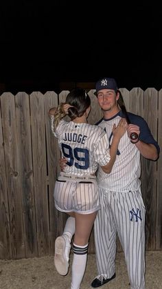 a man and woman in baseball uniforms hugging each other while standing next to a fence