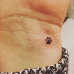 a small dog paw tattoo on the left side of the wrist, it is black and white