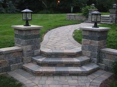 an outdoor walkway with stone steps leading to two lamps on top of each other and grass in the background