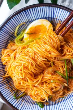 a plate of noodles with chopsticks and an egg