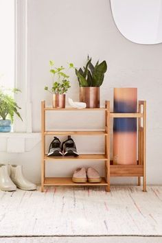 a shelf with shoes, plants and books on it in front of a white wall