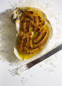 an open oyster shell on some sea salt with a fork and knife next to it