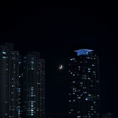 the moon shines brightly in the night sky over some tall buildings