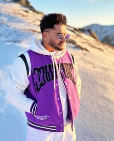 a man with sunglasses on standing in the snow wearing a purple and white hoodie