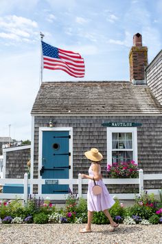 a woman in a straw hat walks past a house with an american flag on the roof