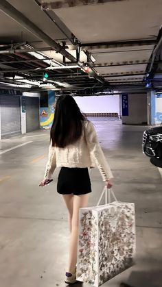 a woman is holding shopping bags and walking in an empty parking garage with no one around