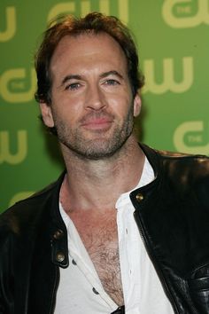 a man wearing a black leather jacket and white shirt smiles at the camera while standing in front of a green background