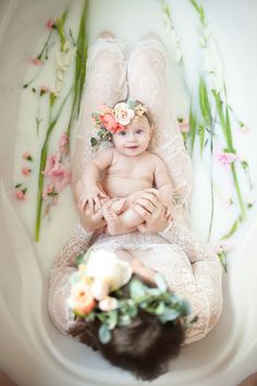 an overhead view of a baby laying on her mother's lap with flowers in her hair