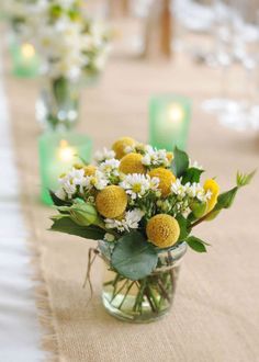 a vase filled with yellow and white flowers sitting on top of a table next to candles