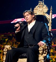 a man in a suit sitting on a chair holding a microphone