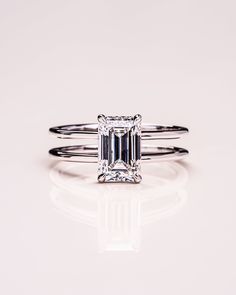 an emerald cut diamond ring with two thin bands on the band, set against a white background