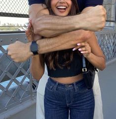 two people hugging each other while standing on a bridge with their arms wrapped around one another