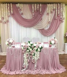 the table is set up with pink and white flowers in front of an elegant drape