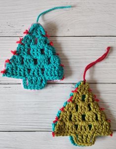 two crocheted ornaments hanging from strings on a white wooden surface, one is green and the other is red