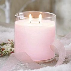 a pink candle sitting on top of snow covered ground next to a white flower and ribbon