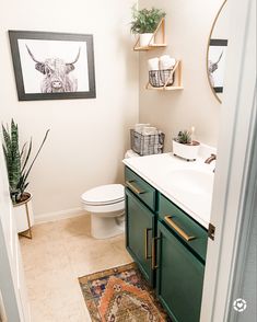 a bathroom with green cabinets and a white toilet next to a framed cow print on the wall