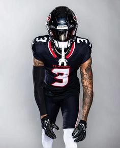 a football player wearing a black uniform and holding a white ball in one hand, with tattoos on the other