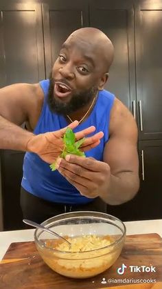 a man in a blue tank top is holding a green leaf over a bowl of food