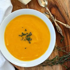 a white bowl filled with soup on top of a wooden table next to silverware