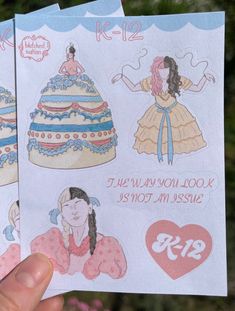 someone holding up two paper dolls with different designs on them, one is wearing a dress and the other has a heart