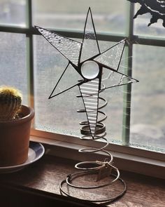 a metal star decoration sitting on top of a window sill next to a potted cactus