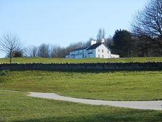 a large white house sitting on top of a lush green hillside next to a stone wall