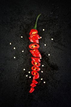 a red hot pepper on a black surface with some white seeds around it and the word food spelled out in cursive letters