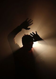 the silhouette of a man with his hands up in front of light coming from behind him