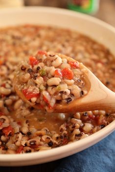 a wooden spoon full of beans and vegetables in a white bowl on a blue cloth