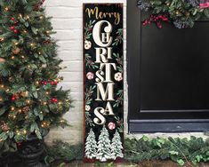 a christmas door hanger with the word merry written on it next to two evergreen trees