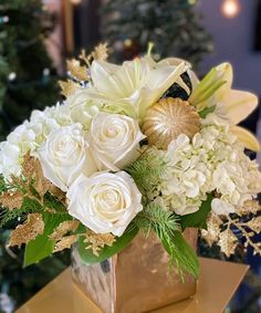 a gold vase filled with white flowers on top of a table next to a christmas tree