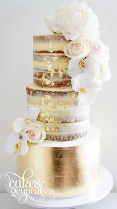 a three tiered cake with white flowers on the top and gold icing around it