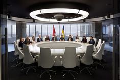 a group of people sitting around a round table with flags on the wall behind them