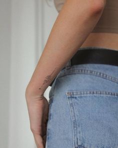 a woman with a tattoo on her left arm is wearing blue jeans and has the word love written in cursive writing