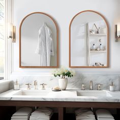 a bathroom with two mirrors above the sinks and white towels hanging on the wall next to it