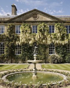 a fountain in front of a large building with lots of windows and plants growing on it