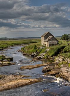 an old building sitting on the side of a river next to a lush green field