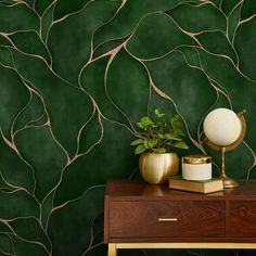 a green wall with gold branches painted on it and a plant next to the table