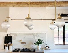 a kitchen with marble counter tops and brass fixtures, hanging lights over the stove top