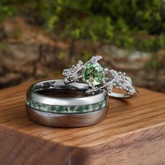 two wedding rings sitting on top of a wooden table next to each other with green and white stones