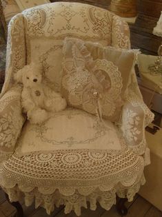 a teddy bear sitting in a chair with pillows on it's back and lace trim around the arms