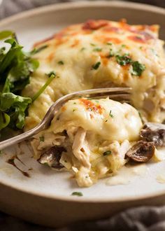 a white plate topped with chicken and mushroom casserole next to a green salad