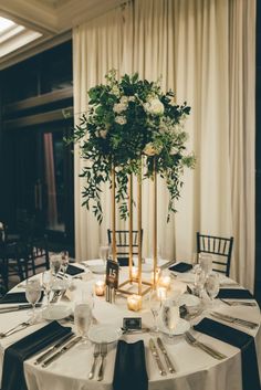 the table is set with white and black linens, silverware, candles, and greenery