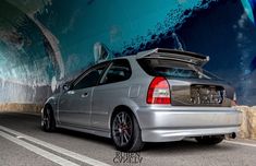 a silver car parked in front of a wall with a painting on it's side