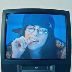 a woman wearing glasses and a hat is on the television screen with her finger in her mouth