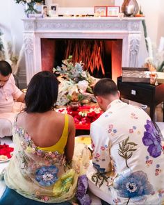 two people sitting on the floor in front of a fire place with flowers all over them