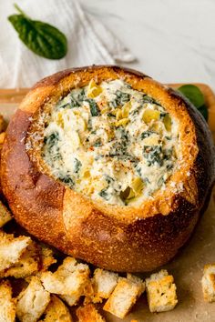 a bread bowl filled with spinach dip surrounded by croutons on a cutting board