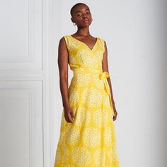 a woman in a yellow dress stands against a white wall